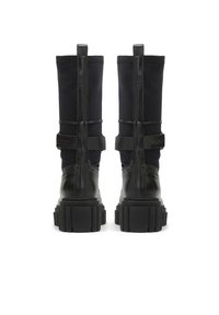 Botines negros con base de cuero liso y caña de tela, con suela de goma gruesa y correas decorativas. Detalles de costura elegantes.