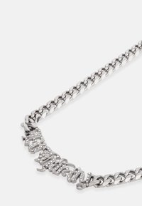 Colar de corrente prateada com uma mistura de elos suaves e texturizados, apresentando um acento decorativo proeminente com texto ornamentado, decorado com pequenas strass.