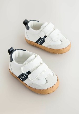 Hvide børnesko med marineblå accenter, to velcrobånd, gummisåler og tekstlabel "BAKER" på siden. Rund tådesign.