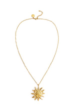 Collar de cadena dorada con un colgante con forma de sol que presenta rayos elevados y texturizados, y una pequeña etiqueta redonda cerca del cierre.