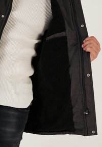 Gray jacket with a black, fuzzy interior lining, featuring a zipper and snap buttons, partially open to show inner pocket detail.
