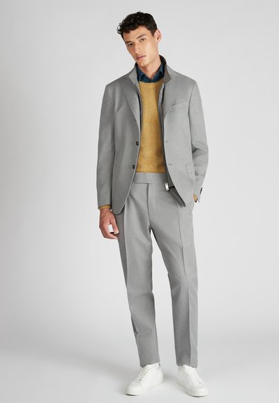 Completo grigio chiaro con rever a lancia, chiusura a un bottone e pantaloni aderenti. Indossato sopra un maglione color senape e completato da sneakers bianche.