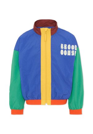 Kurtka w blokach kolorów z niebieskim przodem, zielonymi rękawami, żółtym zamkiem błyskawicznym, brązowym kołnierzem i pomarańczowymi mankietami, z białym stylizowanym napisem na piersi.
