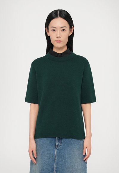 Pull-over en maille vert foncé à manches courtes et col montant, associé à une jupe en denim. Texture lisse, coupe décontractée.