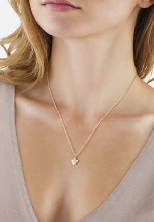 Guldhalskæde med en lille englevedhæng båret om en kvindes hals, vist med lys hud og beige V-hals top.