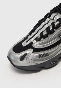 Black and silver athletic shoe with mesh and synthetic materials, featuring a thick sole, dynamic design lines, and "1000" detail on the side.