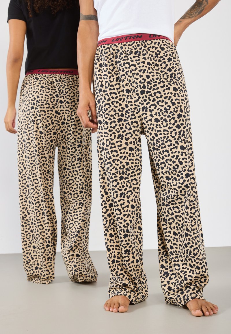 Pysjamasbukser med leopardmønster i beige med sorte prikker, med en rød elastisk talje med "URTRN" trykt. Løs, avslappet passform.