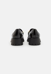 Black patent leather shoes with a chunky black sole, featuring gold hardware accents and a rounded toe design. Smooth texture, sleek finish.
