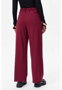 Bordeaux wijde broek met een geassembleerde elastische tailleband en een gladde stoftextuur. Afgewerkt met een ontspannen pasvorm, geschikt voor casual gedragen.