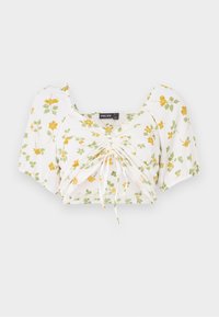 Vit crop top med korta puffärmar, prydd med en gul och grön blommig tryck. Rynkad mittdel med justerbara dragsko för passform.