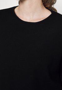 Haut en tricot noir à encolure ronde, texture lisse et coupe ajustée, mettant en avant l'apparence douce du tissu et sa simplicité.