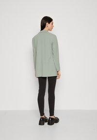 Light green long-sleeve shirt with a pointed collar, paired with black fitted pants and chunky black shoes. Smooth fabric, simple design.