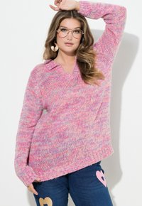 Stickad tröja i rosa, lila och vita nyanser med v-ringning och ribbad fåll. Kombinerad med blå jeans med hjärtdetaljer.