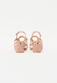 Rosa semskede høyhælte sandaler med åpen bak, kryssbånd og sølvaccent på en kraftig hæl. Glatt tekstur med matt finish.