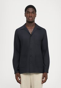 Námorníckou košeľu s golierom, dlhými rukávmi a dvoma prednými náprsními vreckami. Hladká textúra a strih prispôsobený postave.