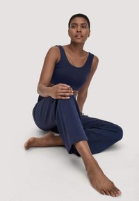 Vrouw met kort haar die op de vloer zit, gekleed in een marineblauw crop top en bijpassende brede broek, en iets omhoog kijkt.