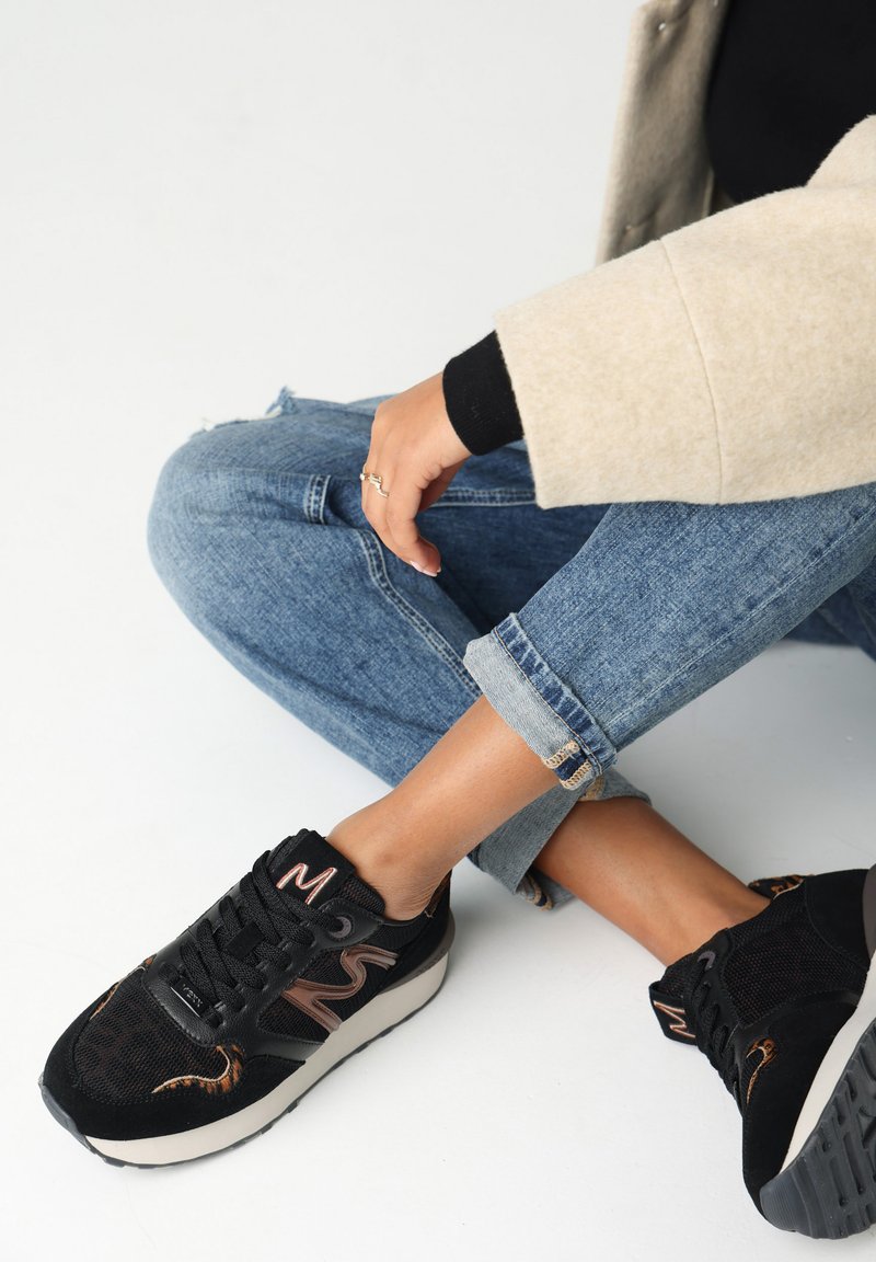 Sneaker nere con tessuto testurizzato e dettagli in pelle, con suola bianca e logo di lato, indossate con jeans blu risvoltati.