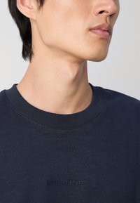 Námornícky modrý bavlnený sweatshirtn s rebrovaným okrúhlym výstrihom a diskrétnym embosovaným logom na hrudníku, ktorý sa vyznačuje hladkou textúrou.