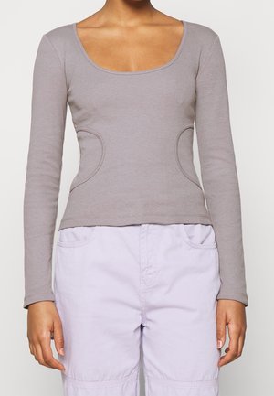 Femme portant un haut gris ajusté à manches longues avec un col rond, associé à un pantalon lavande ample avec poches avant.