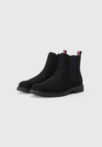 Las botas Chelsea de ante negro cuentan con paneles laterales elásticos y una suela de goma texturizada, con bucles de acento rojo, blanco y azul en la parte trasera.