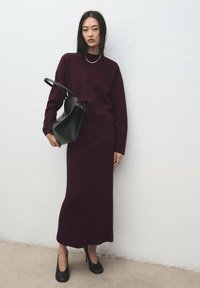 Pulover tricotat burgundy și fustă lungă; geantă structurată neagră; pantofi cu toc înalt negri; texturi netede; design minimalist.