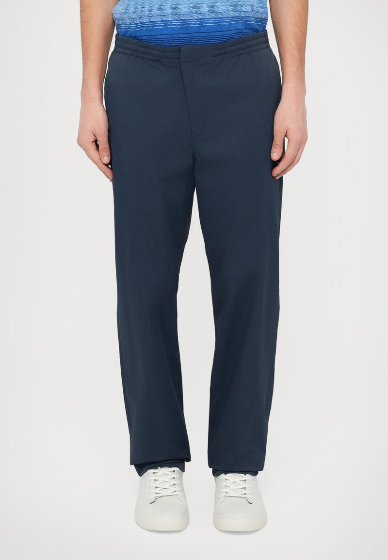 Granatowe spodnie z elastycznym pasem, o prostym kroju i lekkim materiale. Połączone z białymi trampkami dla kontrastu.