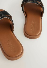 Svarta mockaskinnsandaler med en brun strukturerad sula, med en enkel remdesign och en slät fotbädd. Varumärkets logotyp präglad på innersulan.