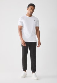 Hvit t-skjorte med korte ermer og en liten gull-logo, parret med svarte joggebukser og hvite sneakers. Glatte teksturer og avslappet passform.
