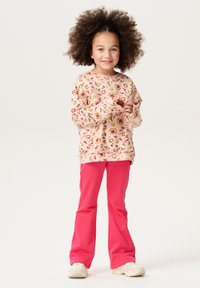 Sweat-shirt à manches longues rose clair avec des motifs de fruits et de fleurs colorés, associé à un pantalon évasé rose vif et des baskets blanches.