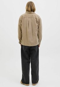 Zachte beige corduroy blouse met een plooidetail, relaxte pasvorm, knopen manchet en achterpand; gecombineerd met losse zwarte denim broek.