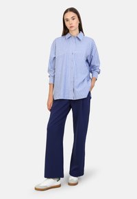 Camicia a righe blu e bianche con colletto, abbinata a pantaloni larghi navy e sneakers bianche con suola in gomma.