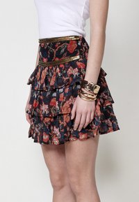 Floral gerimpelde mini-jurk in donkerblauw met rode en groene patronen, gouden pailletten tailleband en gestructureerd gelaagd ontwerp.