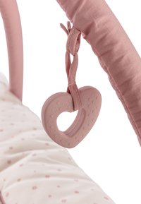 Rosafarbener, herzförmiger Silikonschnuller mit strukturierter Oberfläche, befestigt an einem rosafarbenen Stoffriemen auf einer weichen, gemusterten Babymatte.