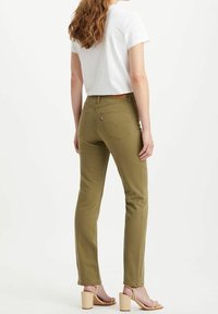 Jeans ajustados en verde oliva con bolsillos traseros, combinados con una camiseta blanca. El modelo lleva sandalias de tacón beige claro.