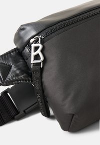 Bolso cruzado negro con un acabado mate texturizado, que presenta un cierre de plata, una correa ajustable y un acento distintivo de hardware plateado.