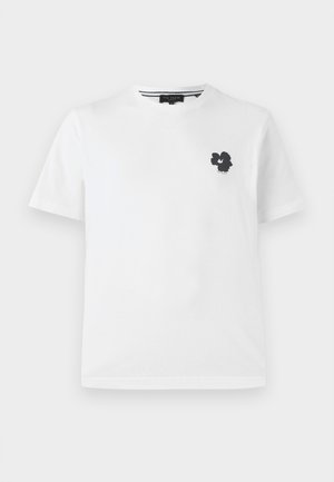 Valkoinen puuvillapaita, jossa on v-pääntie ja pieni musta kukkakuva vasemmassa rinnassa. Lyhyet hihat ja rento istuvuus.