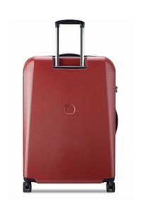 Maleta rígida roja con una superficie texturizada, mango negro extensible y cuatro ruedas para movilidad. Presenta un logotipo circular en la parte trasera.