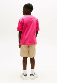 Różowa koszulka z krótkim rękawem o okrągłym dekolcie, w połączeniu z beżowymi szortami. Uzupełniona o białe trampki i prążkowane białe skarpetki.