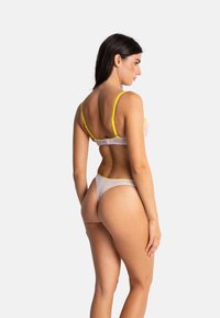 Ensemble de lingerie blanche avec des accents jaunes, comprenant un soutien-gorge avec des straps réglables et un string assorti, mettant en avant un matériau transparent et un design minimaliste.