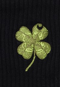 Zielony haftowany czterolistny koniczyna z drobiazgowym ściegiem na czarnym prążkowanym tle.