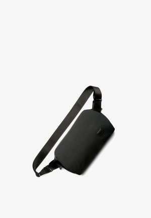 Sacoche noire en tissu durable. Forme rectangulaire avec une sangle en satin et un petit détail logo. Texture lisse, design minimaliste.