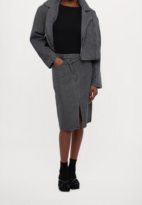 Giacca di jeans grigia dal design corto, abbinata a una gonna di jeans grigia con spacco frontale. Il look è completato da una maglia nera e calzature nere.