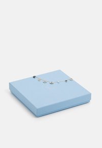 Světle modrá šperkovnice s texturovaným povrchem, která obsahuje stříbrný náramek s různými přívěsky, včetně perly a barevných kamenů.