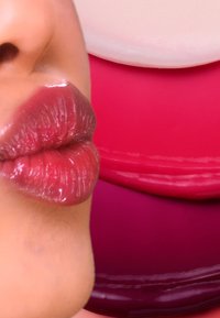 Glanzende, roze getinte lippen in close-up tegen een achtergrond van levendige roze lipproducten, die een gladde textuur en subtiele glans tonen.