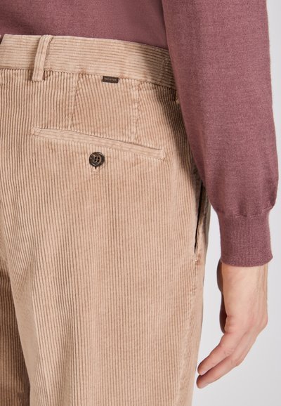 Światło brązowe spodnie w korduroy z pionowymi prążkami, z tylną kieszenią i ciemnym guzikiem. Stylizowane z fioletowym swetrem.