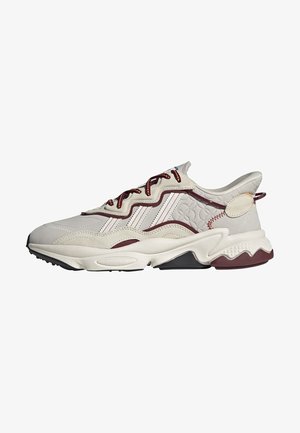 Witte en bordeaux sneaker met getextureerd zijpaneel, golvend ontwerp, dikke zool en veters met bordeaux accenten, gezien vanaf de buitenzijde.