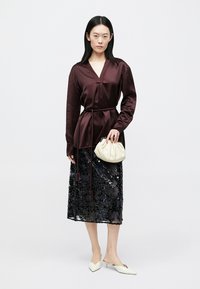 Bourgognefarvet satin langærmet bluse med V-hals og bælte i taljen; sort paliet-midi-nederdel; hvidt tekstureret clutch-tasker; spidse hvide hæle.