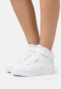 White high-top sneakers with a textured leather finish, padded collar, flat laces, and a gold Puma logo on the side. Thick rubber sole.