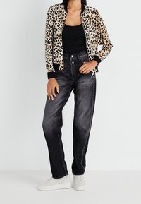 Chaqueta bomber con estampado de leopardo y puños negros, combinada con vaqueros oscuros de cintura alta y zapatillas blancas. Texturas suaves y patrones audaces.