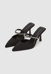 Des escarpins noirs à bout pointu en tissu lisse, dotés une bride ornée de strass et d'un talon fin et effilé.